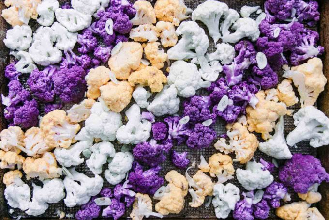 white, purple, and orange cauliflower arranged in colorful lines on a baking sheet