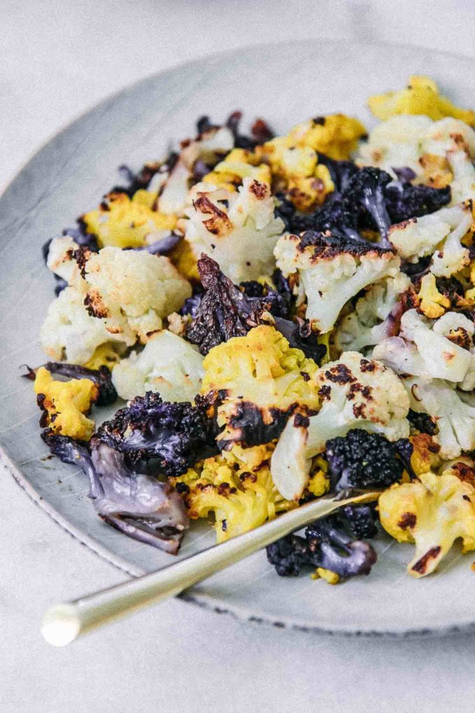 a close up photo of roasted rainbow colored cauliflower florets, white, green, and orange, on a white plate