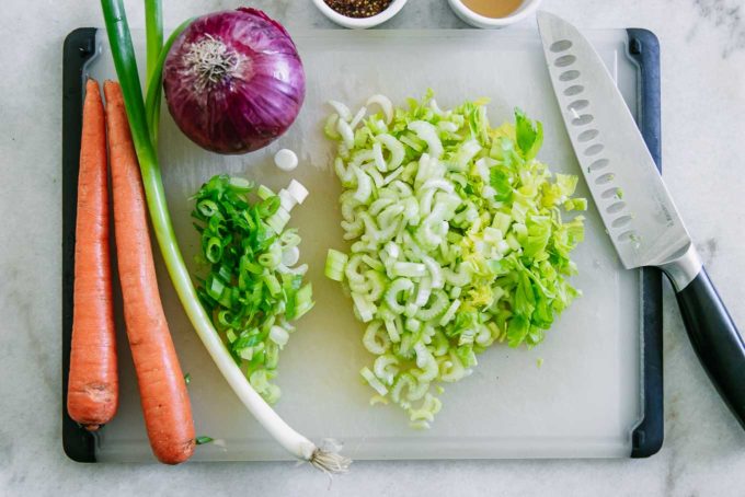 cut celery and green onions with carrots on a white cutting board