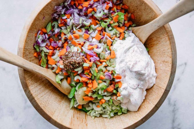 potatoes, celery, carrots, green onions, and vegan mayonnaise in a large wooden mixing bowl