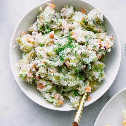 a white bowl with plant-based potato salad and a gold fork on a white table