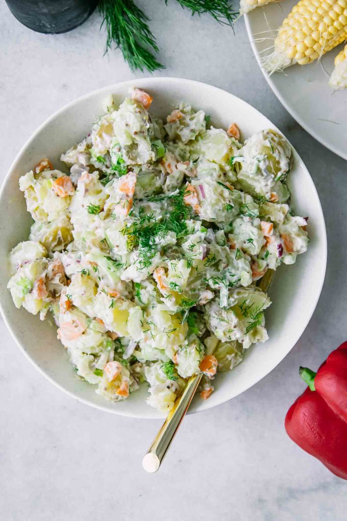 vegan potato salad in a white bowl with a gold fork on a white table