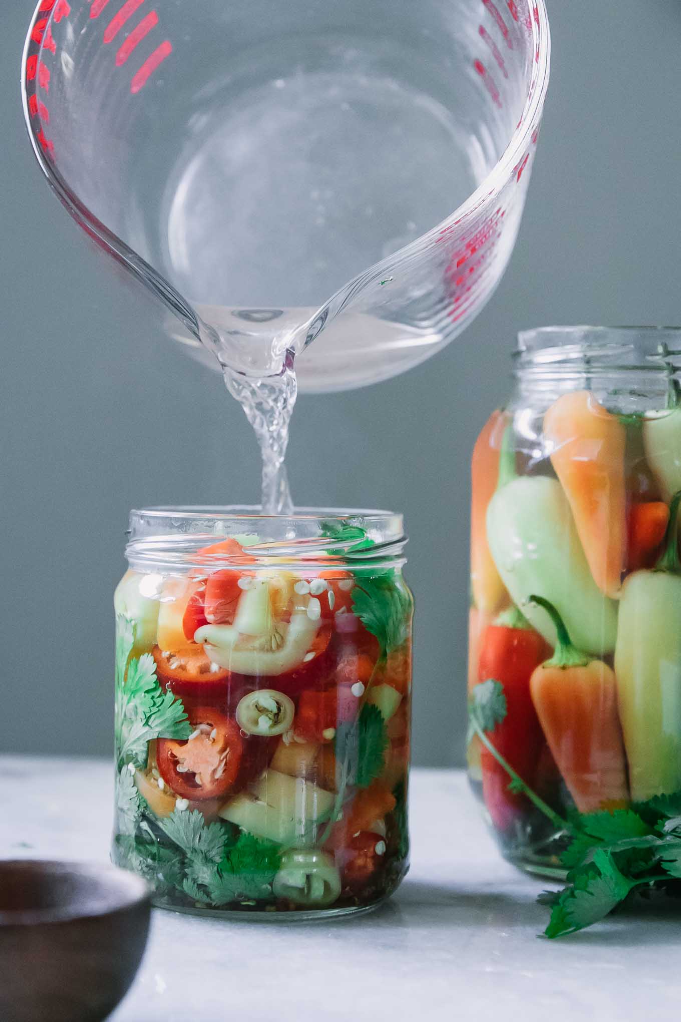 pickling brine pouring into a jar of sliced peppers