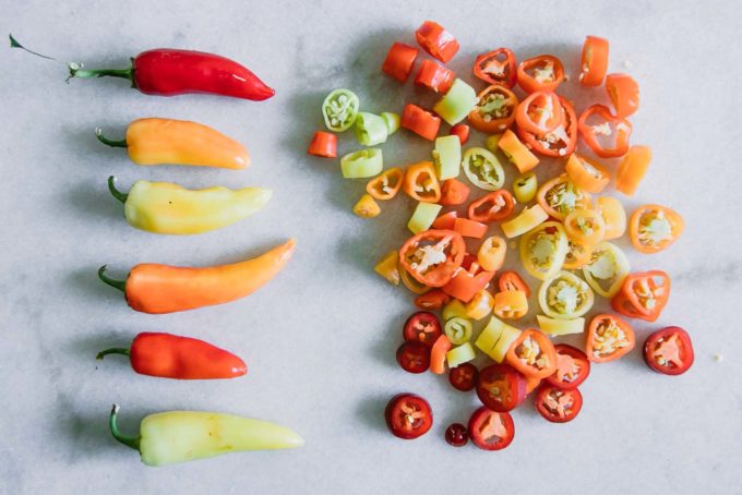 whole and sliced red, orange, and yellow peppers on a white table