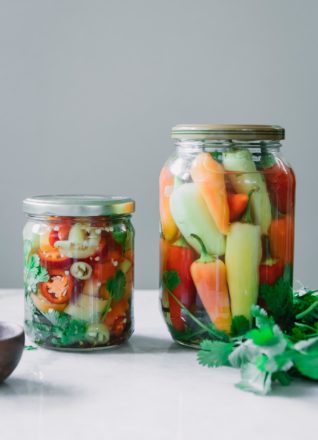 two jars of pickled peppers, one with sliced peppers and one with whole peppers