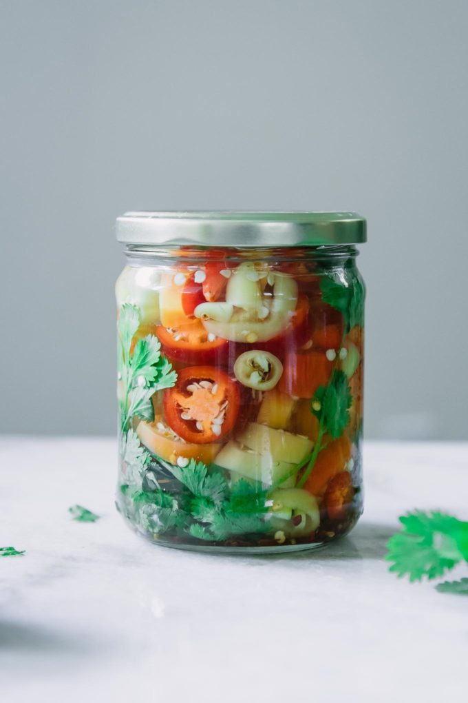 a jar of sliced pickled red, orange, and yellow peppers on a white table