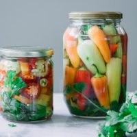 two jars of pickled peppers on a white table with fresh cilantro