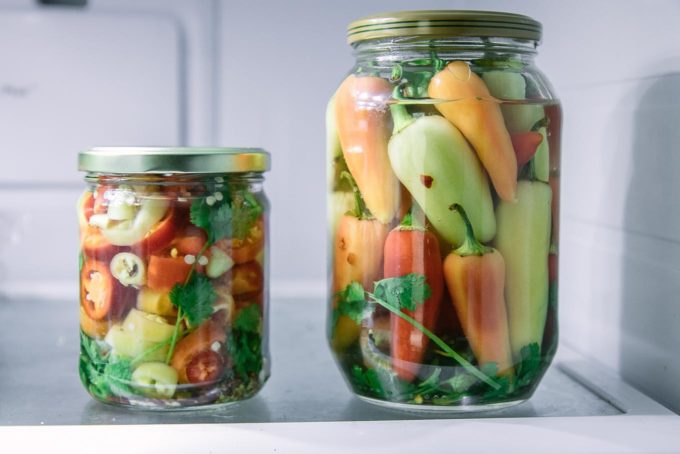 two jars of sliced and whole pickled peppers on a refrigerator shelf