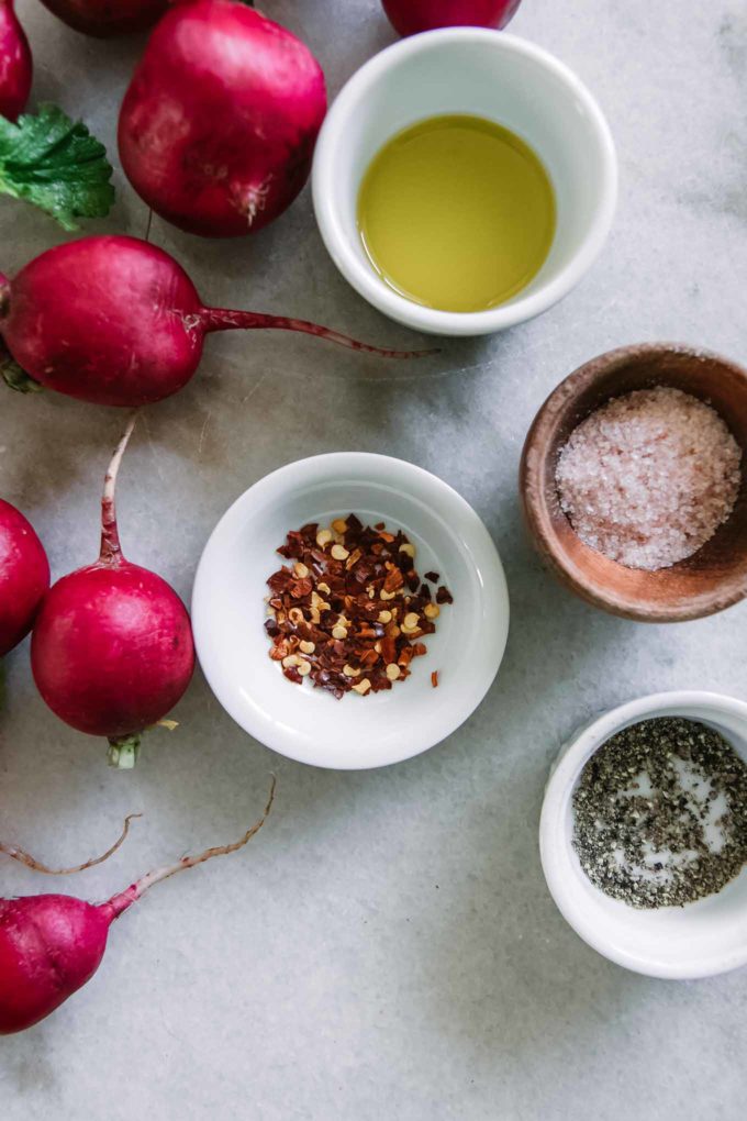 bowls of olive oil, sea salt, black pepper, red pepper flakes, and red radishes on a white table
