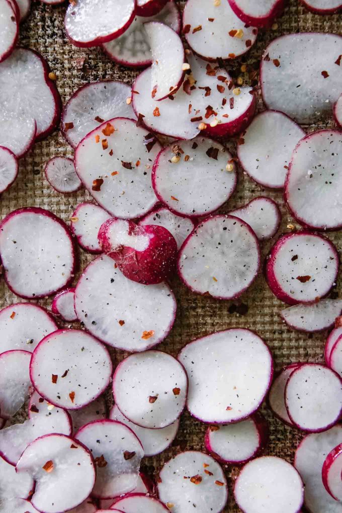 sliced radishes on a baking sheet with olive oil, salt, and pepper