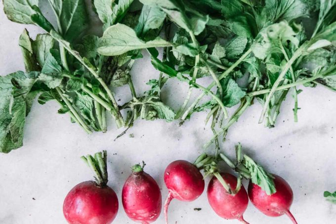 radish bulbs cut from the green radish stems and leaves on a white table