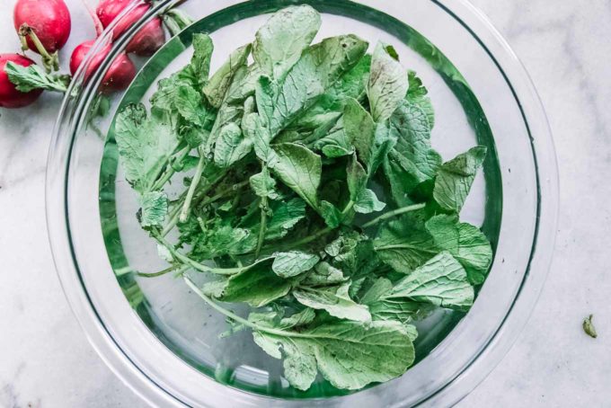 radish greens in a bowl of water on a white table