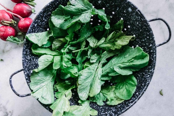 radish greens in a blue colander on a white table