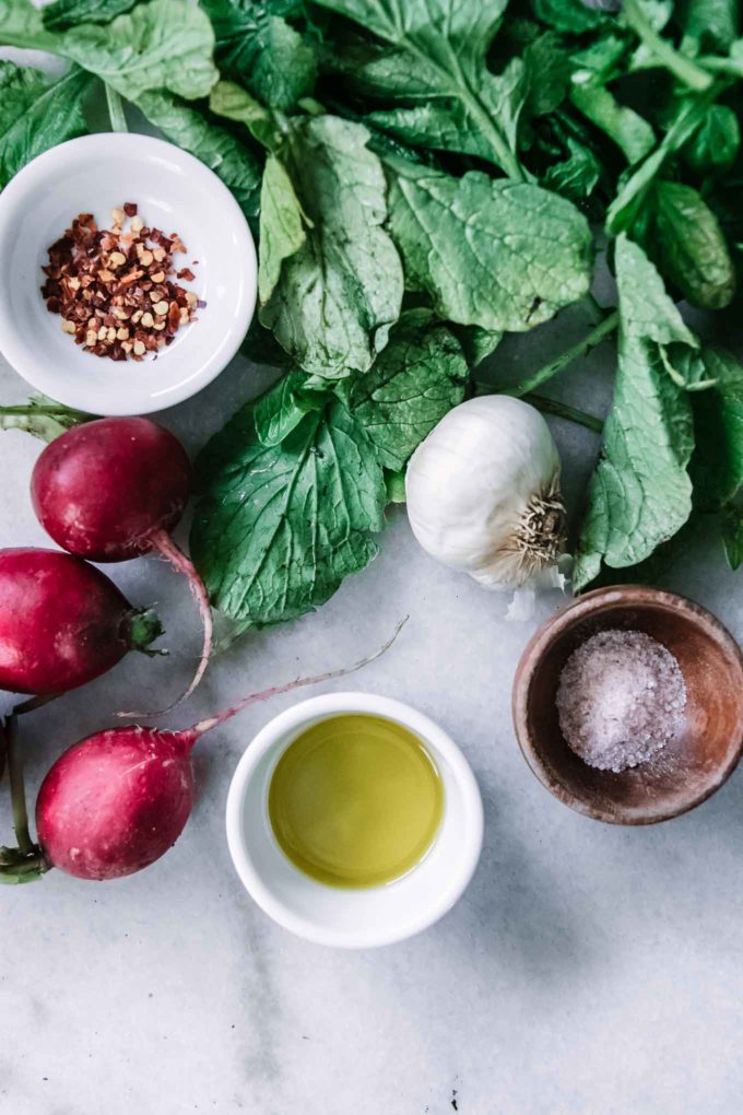 radish greens, garlic, and bowls of olive oil, sea salt, and red pepper flakes on a white table