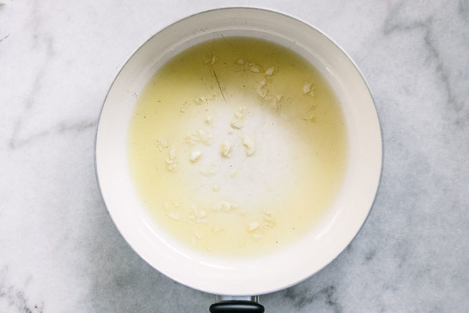 olive oil and sliced garlic in a white pan on a white table