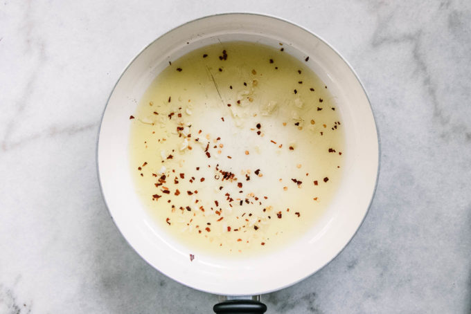 olive oil, minced garlic, and red pepper flakes in a white pan on a white table