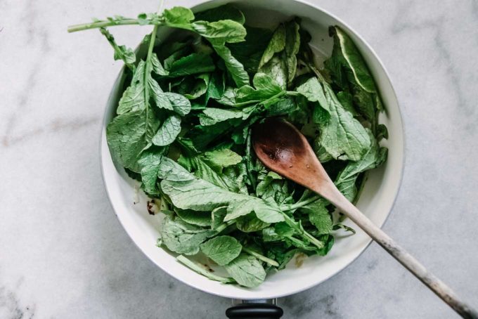 radish greens in a white pan with a wooden spoon