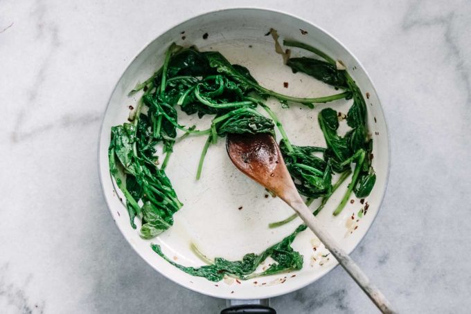 cooked radish leaves in a white pan with a wooden spoon