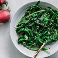 sauteed radish greens in a blue bowl with a gold fork