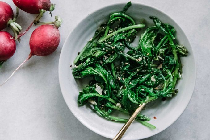 sauteed radish greens in a blue bowl with a gold fork