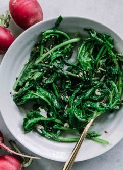 sauteed radish greens in a white bowl with a gold fork