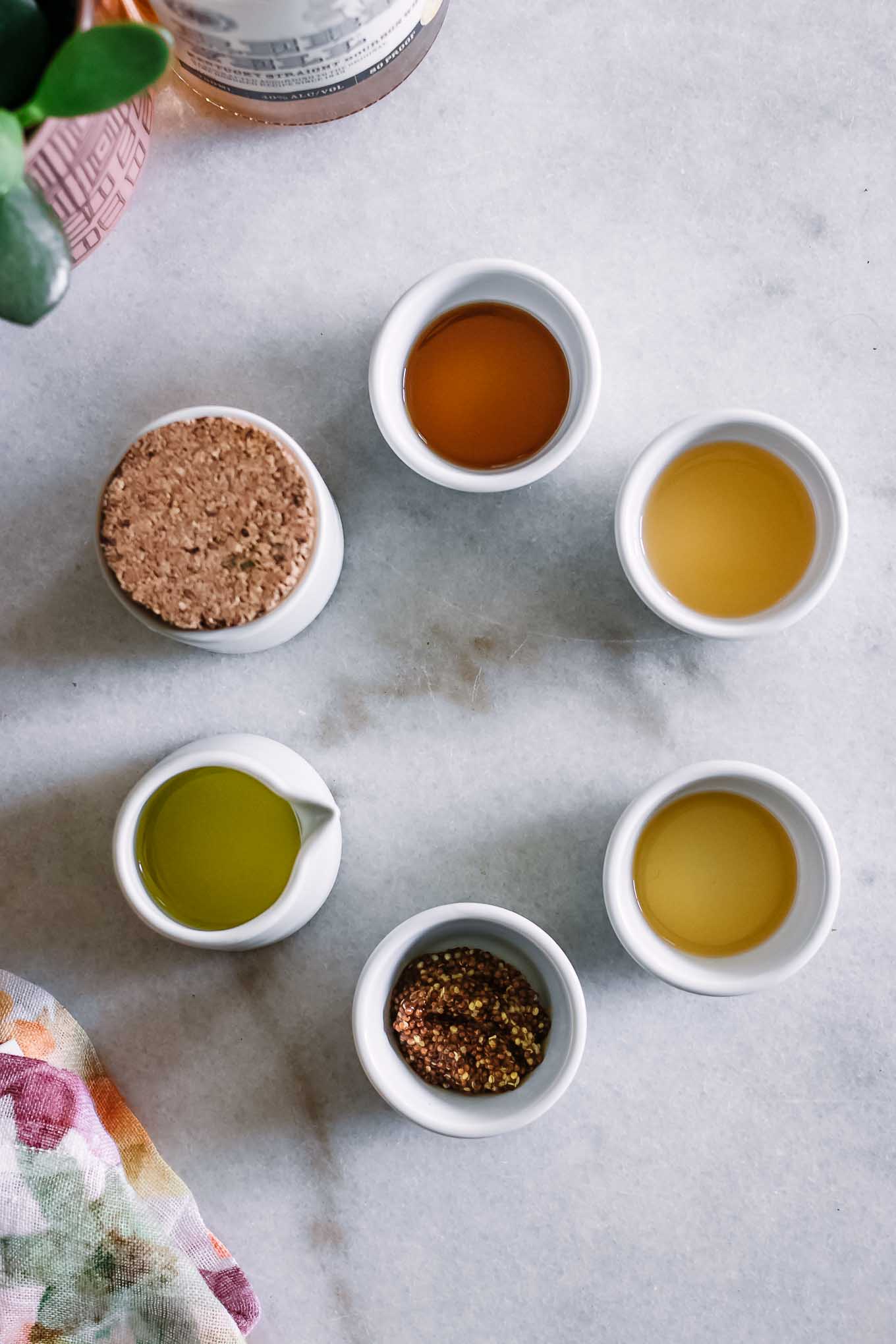 bowls of olive oil, vinegar, maple syrup, bourbon whiskey, salt, and mustard on a marble countertop