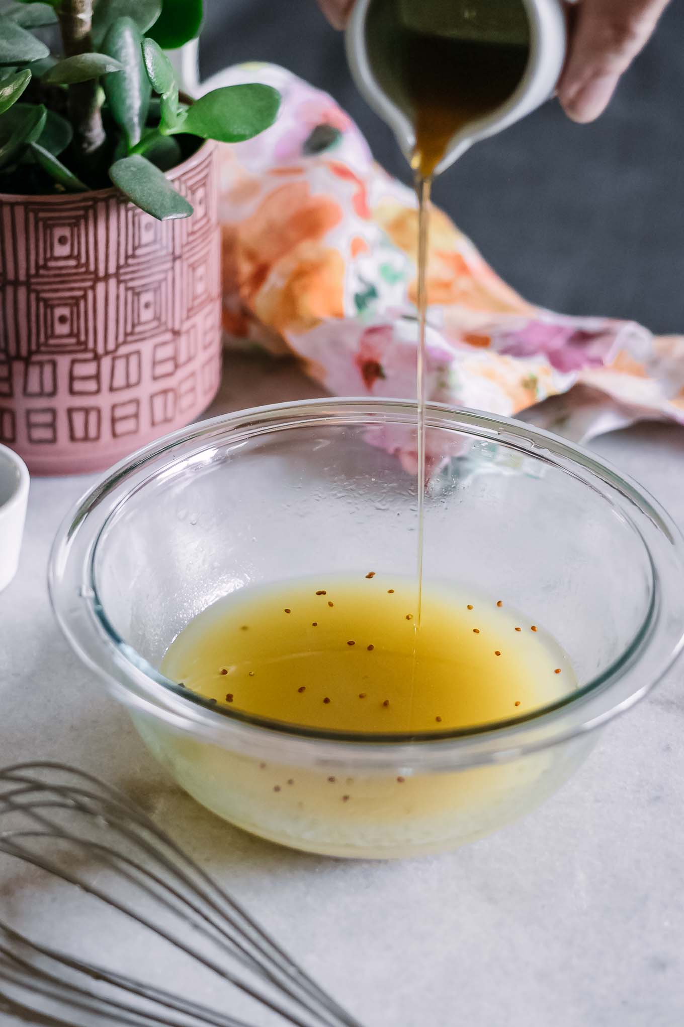 a hand pouring maple syrup into a glass bowl with oil and vinegar