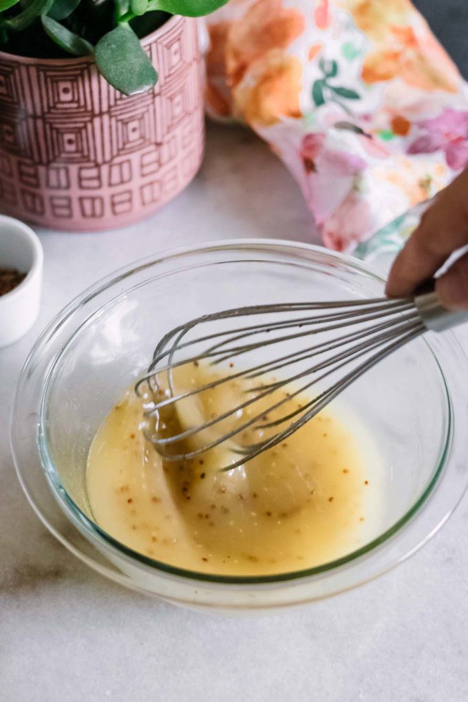 a hand whisking salad dressing in glass mixing bowl
