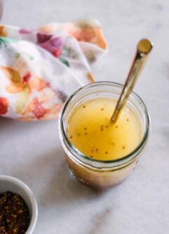 a mason jar with vinaigrette salad dressing on a white table with a gold spoon