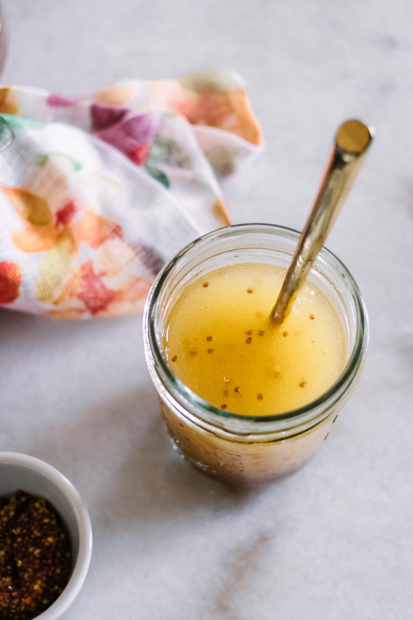 a mason jar with vinaigrette salad dressing on a white table with a gold spoon