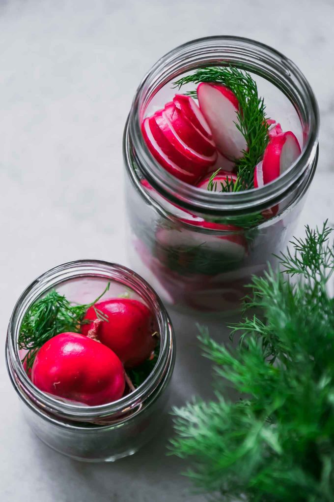 sliced and whole radishes in glass jars with fresh dill