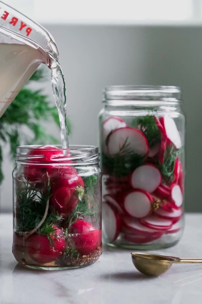 vinegar pickling brine pouring into a jar of radishes