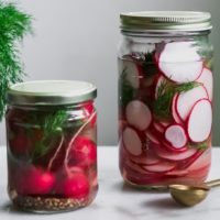 two jars of sliced and whole pickled radishes on a white table