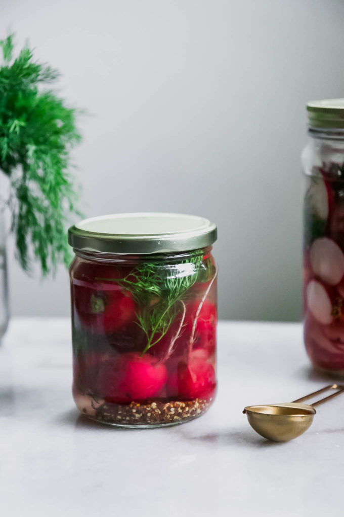 a jar of whole pickled radishes on a white table with fresh dill