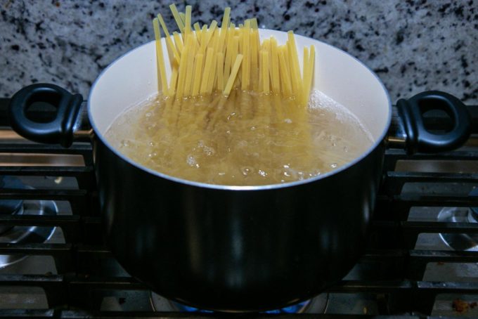 a black pot of boiling water with pasta on a stovetop