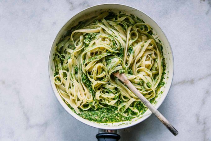 pesto pasta in a white pan with a wooden spoon