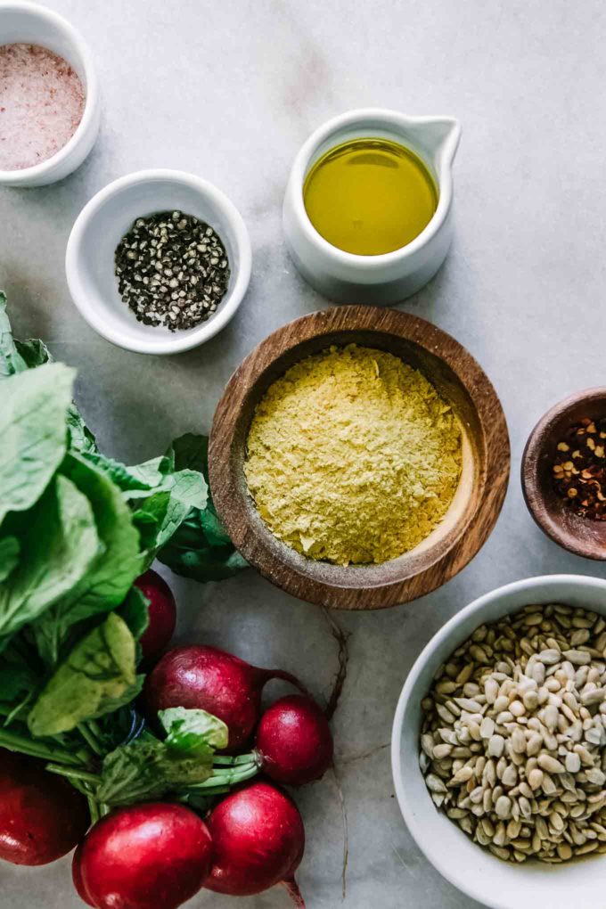 bowls of cheese, sunflower seeds, olive oil, salt, and pepper with a bunch of radishes on a white table