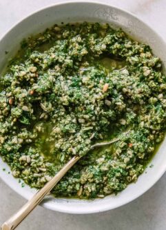 pesto sauce made from radish greens in a white bowl with a gold fork and radishes on a white table