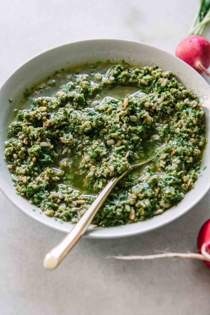 a bowl of pesto sauce with a gold fork and radishes on a white table