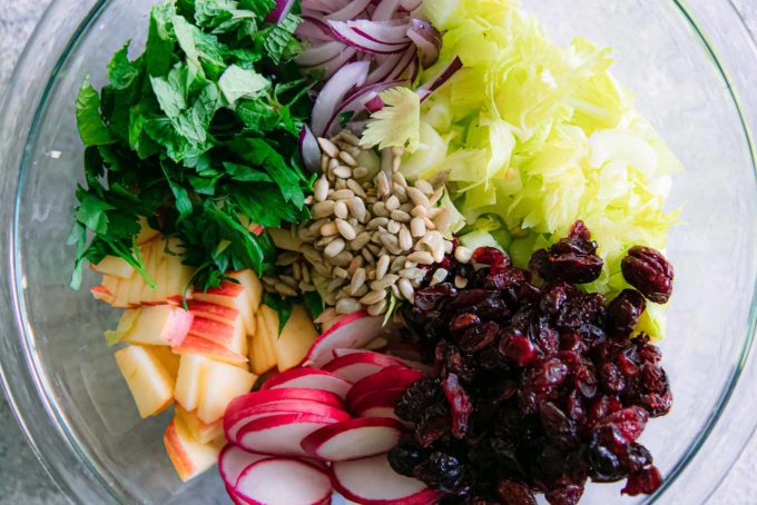 chopped celery, apple, radish, cranberries, herbs, and onion in a glass mixing bowl