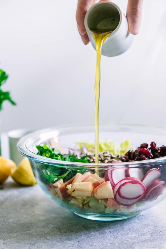 a hand drizzling salad dressing to a bowl with salad ingredients