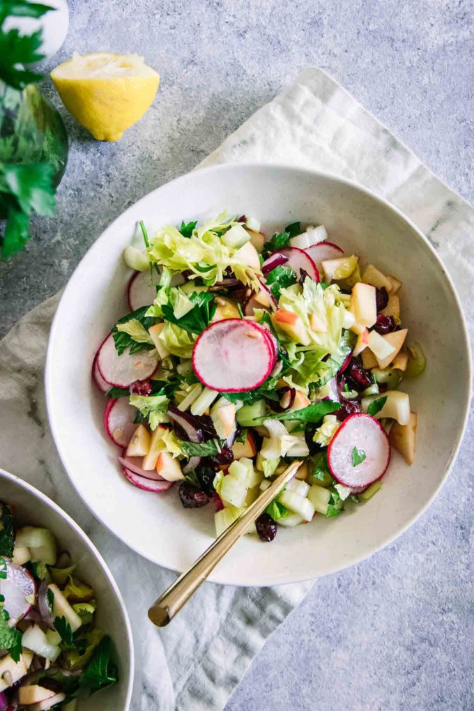 two white bowls with a celery and apple salad on a blue table