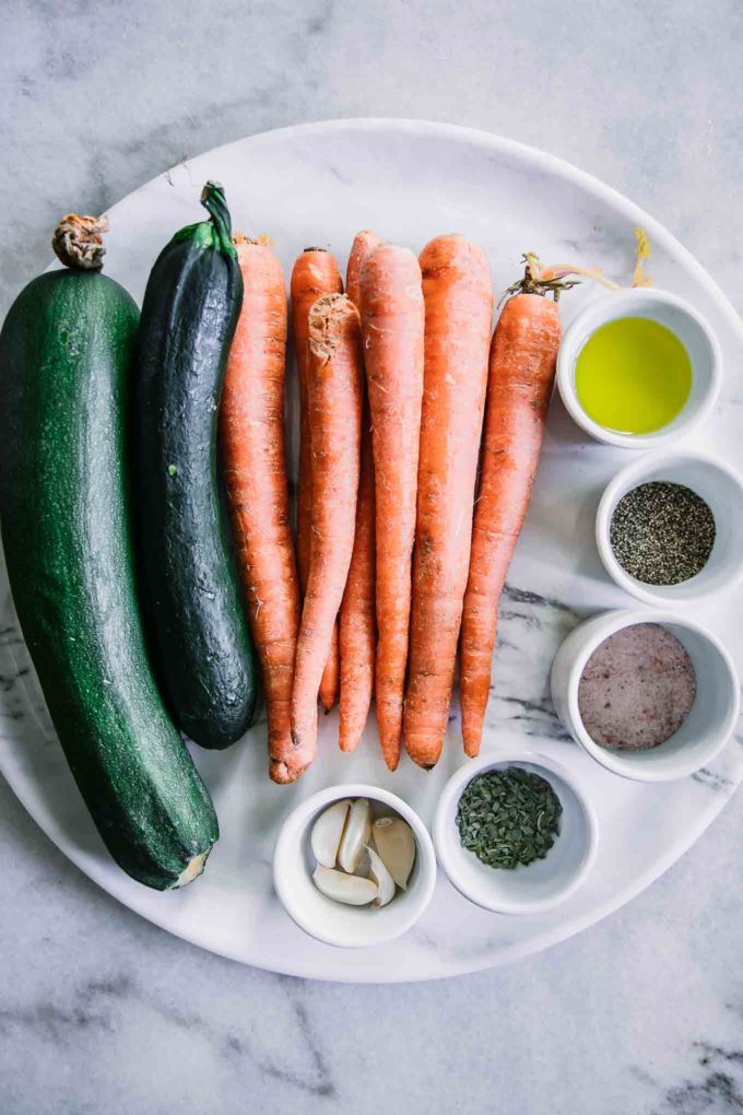 zucchini, carrots and small bowls of oil and spices on a white marble countertop