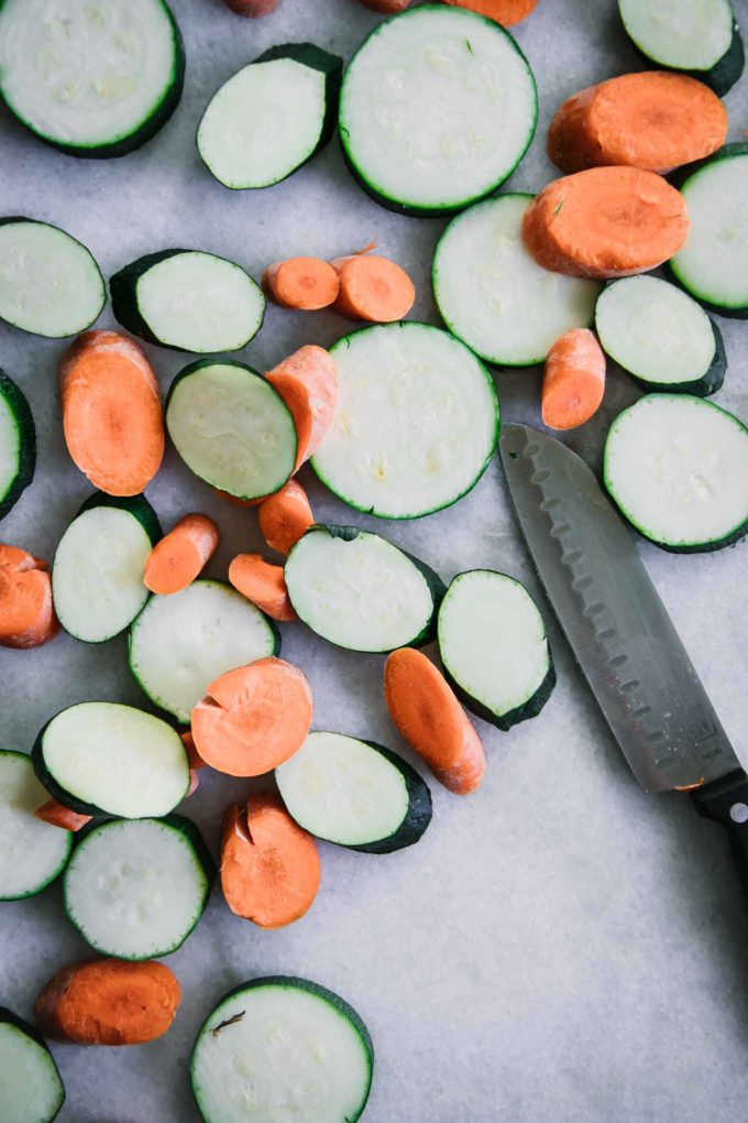 sliced carrot and zucchini rounds on a white table with a knife