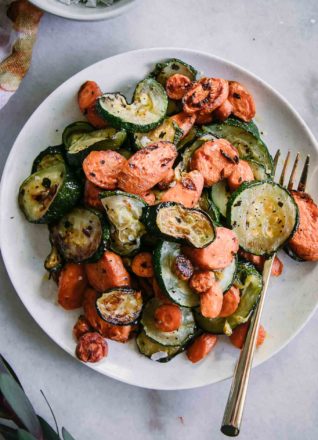 roasted sliced carrots and zucchini on a white plate with a gold fork
