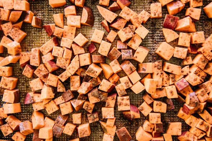 cut sweet potatoes on a baking sheet with cinnamon and maple syrup