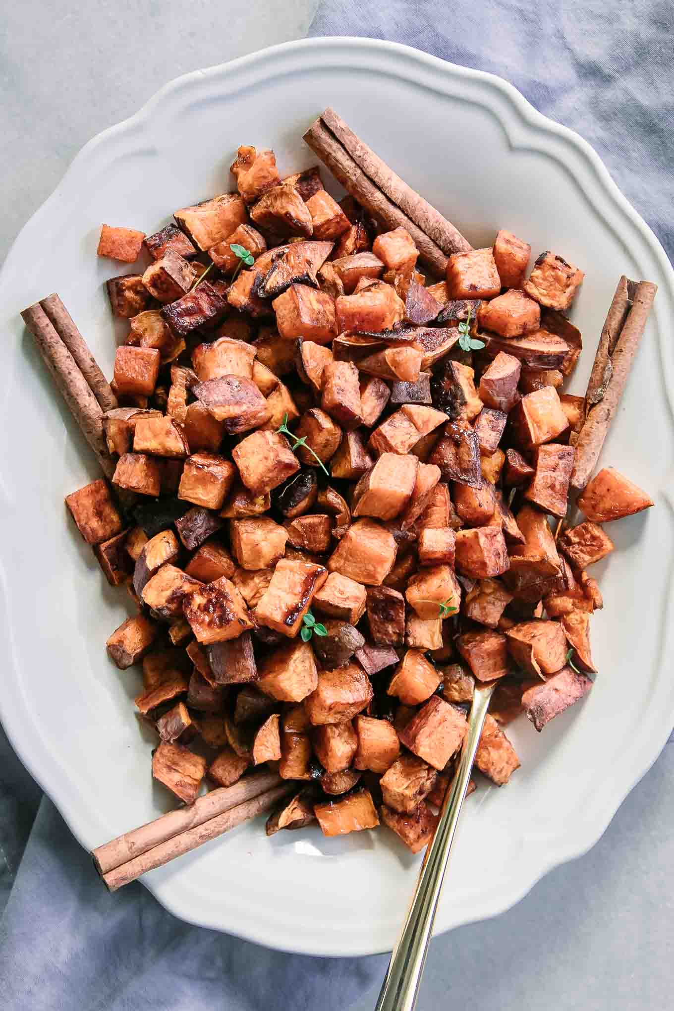 roasted sweet potatoes and cinnamon sticks on a white plate with a gold fork
