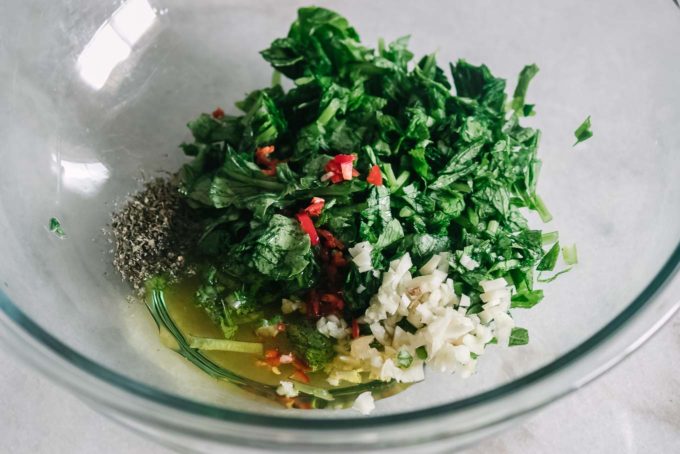 chopped radish greens, garlic, peppers, oregano, and olive oil in a glass mixing bowl