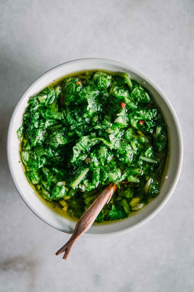 a bowl of green chimichurri on a white table