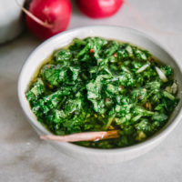 a bowl of chimichurri on a white table with radishes and lemons